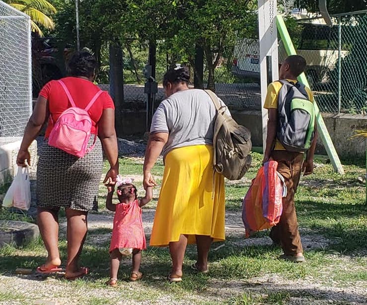 Two women walking, holding the hands of a toddler between them