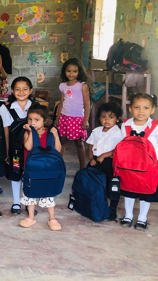 Children in school uniforms pose with their new backpacks