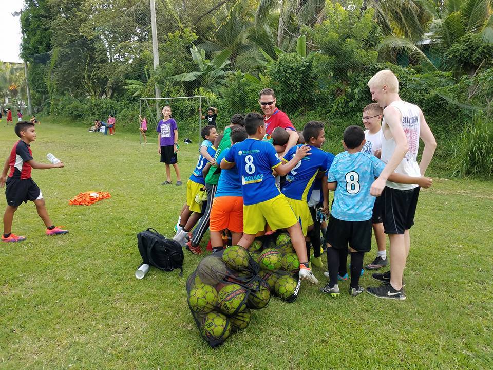 Teenage boy being hugged by a group of young children in soccer uniforms