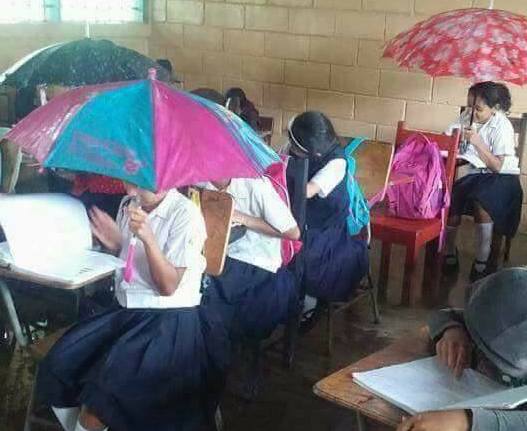 Children using umbrellas in school because the roof is leaking